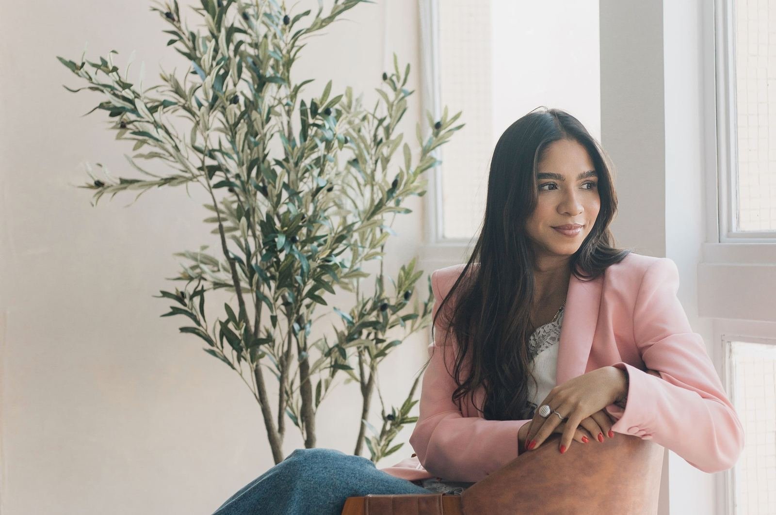 Vanessa Tavares sentada perto da janela, com blazer rosa