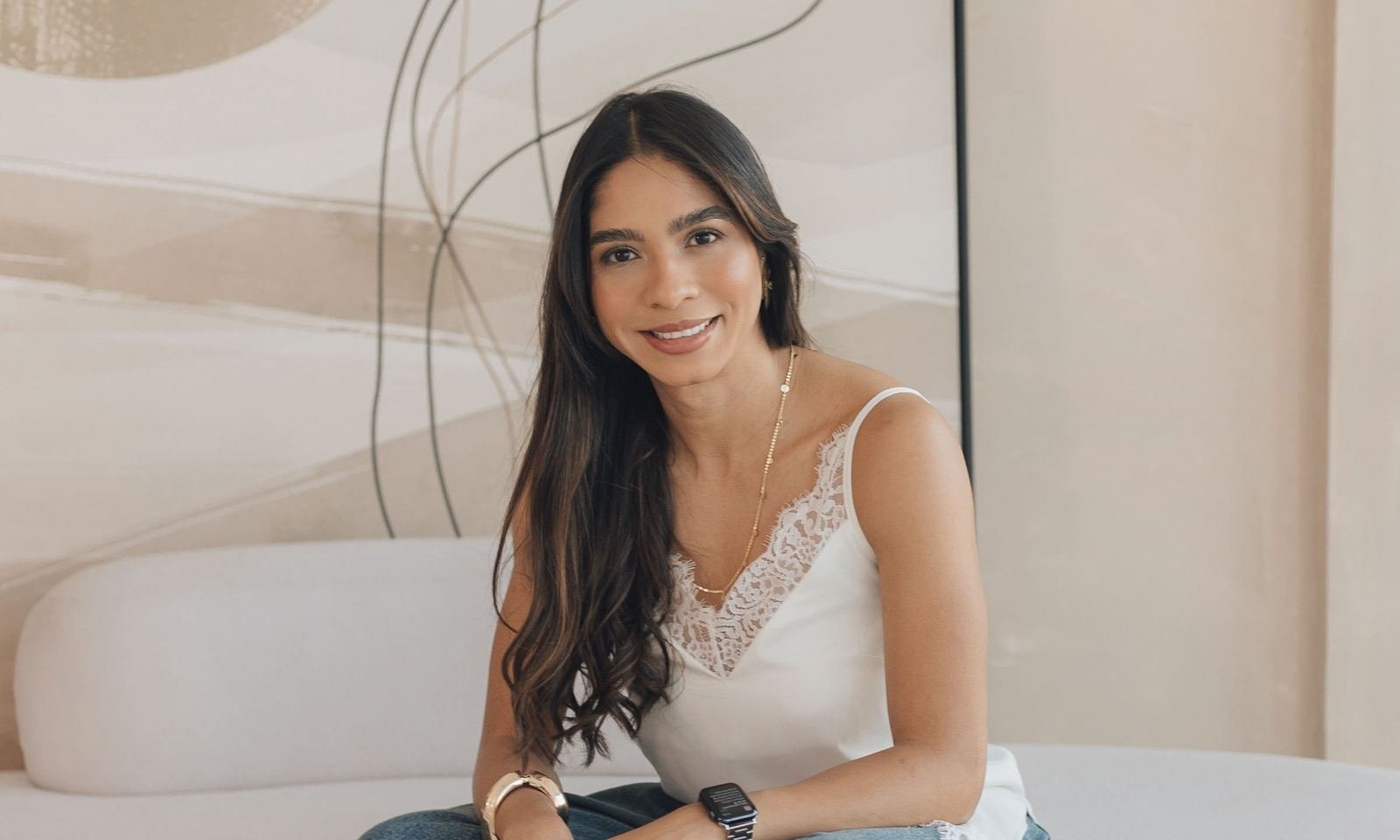 Vanessa Tavares sorrindo, sentada em um sofá claro